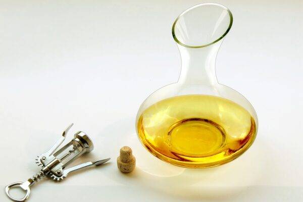 Picture of a wine decanter with white wine and corkscrew.