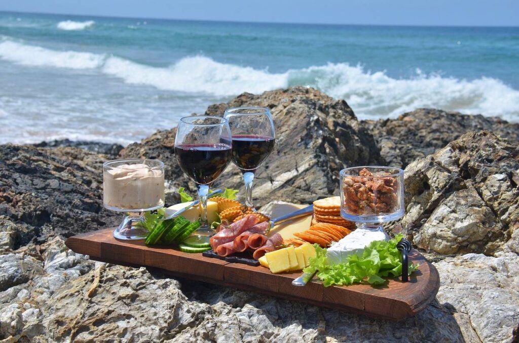 A photo of a cheese platter with wine by the sea.